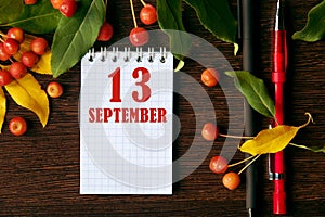 calendar date on wooden dark desktop background with autumn leaves and small apples. September 13 is the thirteenth day of the