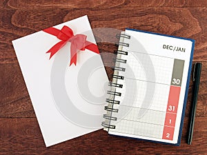 calendar diary planner with date of December and January in grid and envelope with red ribbon bow and pen on desk floor