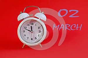 Calendar en March 2: white alarm clock on a crimson background close-up, numbers 02, the name of the month March in English