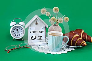 Calendar for February 1: a decorative house with the name of the month in English, numbers 01, homemade cakes, a cup of tea, a