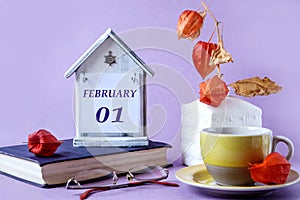 Calendar for February 1: the name of the month in English, the numbers 01, a yellow cup of tea, a physalis branch in a vase, a