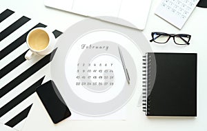 Calendar of February on white desktop flat ley with a cup of coffee and a notebook