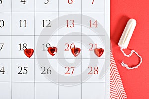 Calendar of the female menstrual cycle with pads and tampons on a red background.