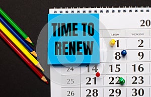 The calendar has light blue note paper with the text TIME TO RENEW. Nearby colored pencils on a dark background. View from above