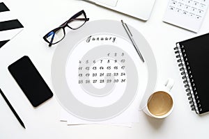 Calendar of January on white desktop flat lay with a cup of coffee and a notebook white work space