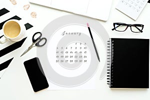 Calendar of January on white desktop flat ley with a cup of coffee and a notebook workspace