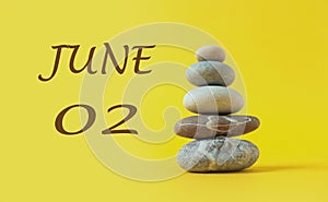 Calendar for June 2: numbers 02, the name of the month June in English, a pyramid of sea pebbles, yellow background