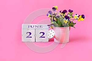 Calendar for June 22 : the name of the month of June in English, cubes with the number 22, a bouquet of violets in a pink watering