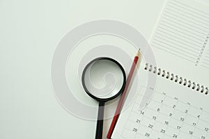 Calendar and magnifying glass on the white table background, planning for business meeting or travel planning concept