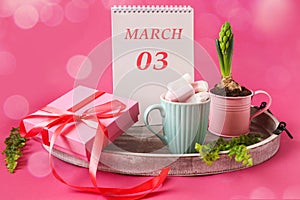 Calendar for March 3: a notepad with the inscription 03 March in English, blooming hyacinth, air marshmallow in a cup, a gift tied