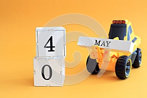 Calendar for May 4: a toy yellow tractor with numbers on cubes 0 and 4, the name of the month in English on a yellow background