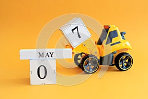 Calendar for May 7: a toy yellow tractor with numbers on cubes 0 and 7, the name of the month in English on a yellow background