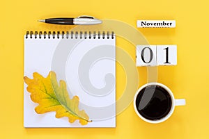 Calendar November 1 cup of coffee, notepad with pen and yellow leaf on yellow background