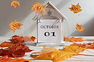 Calendar for October 1 : decorative house with numbers 01 and the name of the month in English, falling maple leaves , gray