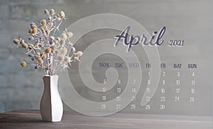 Calendar-page for the full month: April 2021. A composition of dried flowers in a white porcelain vase on a wooden table. The