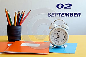 Calendar for September 2: numbers 02, the name of the month September in English, a white alarm clock, school supplies on the