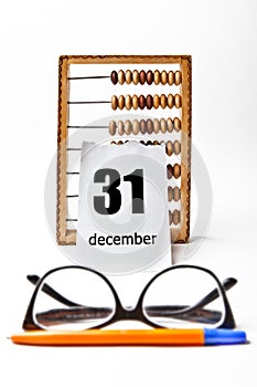 Calendar sheet with the date of 31 December with a wooden abacus on near the glasses and pen.