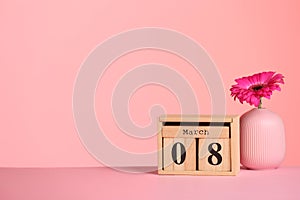 Calendar and vase with flower on table against color background, space for text.