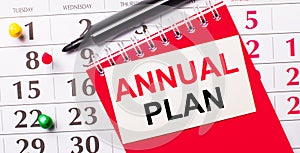 On the calendar is a white card with the text ANNUAL PLAN. Nearby is a red notepad and a marker. View from above