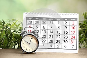 Calender and alarm clock on wooden table against green background