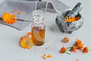 Calendula products. Bottle of cosmetic, aromatic or essential oil and fresh and dry calendula flowers on light background.