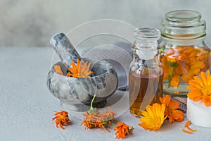 Calendula products. Bottle of cosmetic, aromatic or essential oil and fresh and dry calendula flowers on light background.