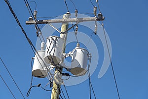 Overhead transformer bank with three white distribution transformers on pole with blue sky