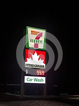 A sign of a Seven Eleven, Petro Canada with the price of gas and a Car Wash sign at night. A