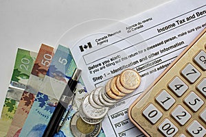 Canadian Tax Forms with coins, calculator, a pen and bills on a white table. Tax time