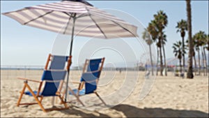 California beach defocused, two empty blue deck chairs, striped umbrella near pier in Santa Monica pacific ocean resort