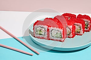 California maki roll with tobiko caviar on modern coloured background. Sushi roll with crab and cucumber inside, tobiko caviar