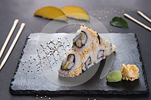 California roll with sesame. Roll with shrimp and mango. Japanese food. Roll on a black shale with Japanese sticks