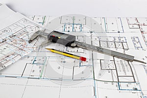A caliper and a pencil lie on a fragment of a construction drawing.