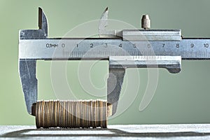 Calipers and stack of coins close-up against green wall.