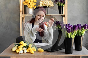 A call center agent with a headset works on a hotline behind a laptop. female florist in flower shop near showcase with