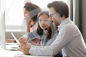 Call center agents in headsets discussing papers helping at workplace