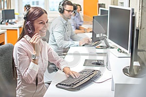Call center business woman talking on headset in row with her colleagues in office.