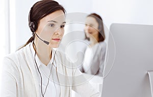 Call center. Casual dressed woman sitting in headset at customer service office. Group of operators at work. Business