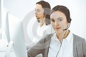 Call center. Casual dressed woman working in headset with diverse colleagues at office. Business concept