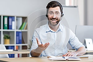 Call center employee talking to customer smiling and looking at webcam, man with headset for video call