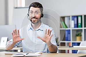 Call center employee talking to customer smiling and looking at webcam, man with headset for video call