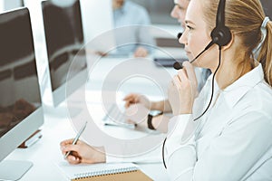 Call center. Group of casual dressed operators at work. Blond business woman in headset at customer service office