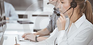 Call center. Group of casual dressed operators at work. Blond business woman in headset at customer service office