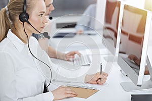 Call center. Group of casual dressed operators at work. Blond business woman in headset at customer service office