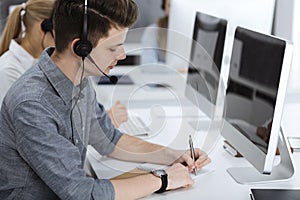 Call center. Group of casual dressed operators at work. Businessman in headset at customer service office. Telesales in