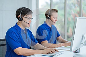 Call center man in blue shirt uniform working care customer service wearing headphone talking with customer at call center office