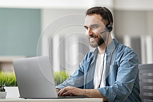 Call center operator. Handsome male manager wearing headset and typing on laptop