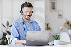 Call center operator at work. Male manager wearing headset and using laptop