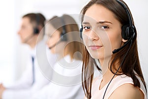 Call center operators. Focus on young cheerful smiling woman in headset. Business and customer service concepts