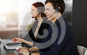 Call center operators at work. Two young people in headsets are talking to the clients, while sitting in sunny office